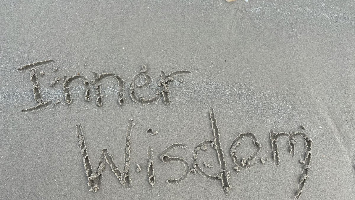 Message 'Inner Wisdom' written on sand at a Scottish beach, surrounded by seashells.