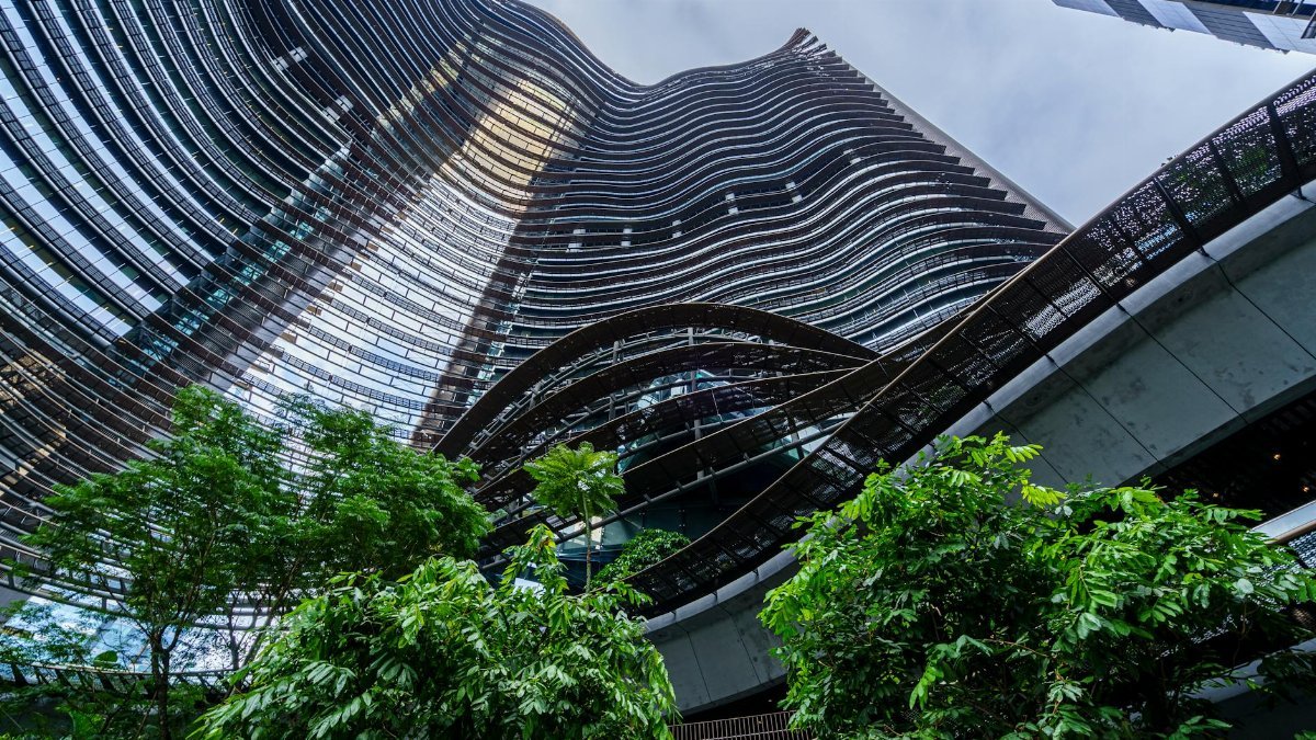 Wavy architectural design of a modern glass skyscraper amidst lush greenery.