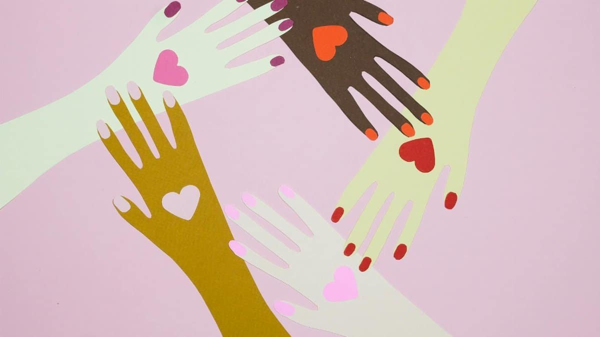 Artistic paper cutout hands with hearts symbolize unity and love on a pink background.