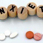 Wooden blocks spelling 'Anxiety' with assorted pills below on a light background.