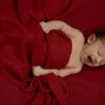 A cute newborn baby peacefully yawns while wrapped in a soft red blanket, evoking warmth and tranquility.