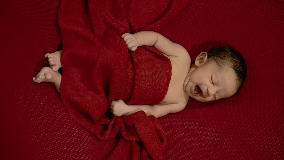 A cute newborn baby peacefully yawns while wrapped in a soft red blanket, evoking warmth and tranquility.