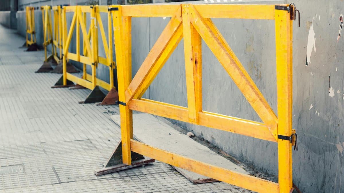 Multiple yellow construction barriers line a sidewalk outdoors, creating a linear pattern.