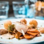 Beautifully plated scallop dish with vegetables and fries in a French restaurant setting.