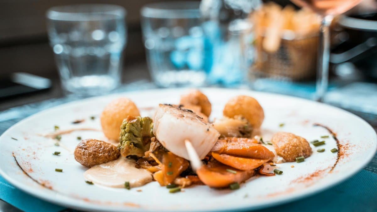 Beautifully plated scallop dish with vegetables and fries in a French restaurant setting.
