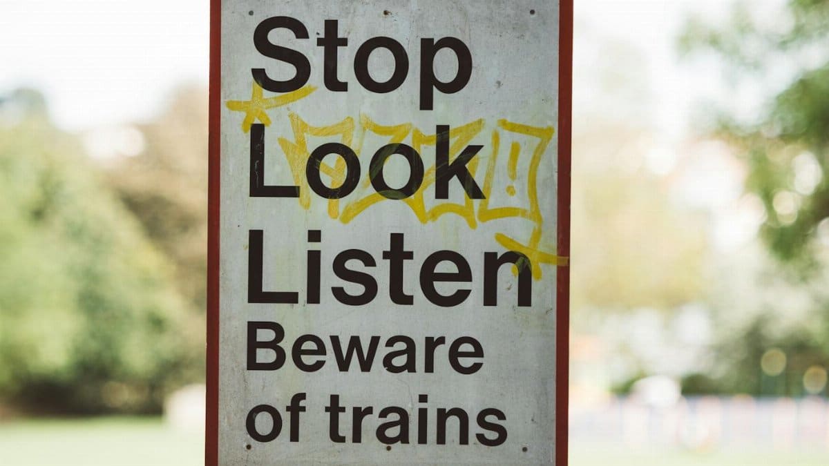Rectangular signboard with Beware Of Trains title on post near city park in daytime