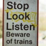 Rectangular signboard with Beware Of Trains title on post near city park in daytime