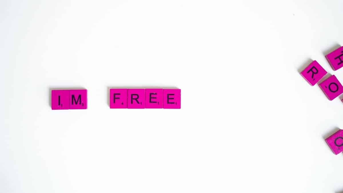 Pink scrabble tiles with the text 'I'M FREE' on a white surface, offering a symbolic message of freedom.