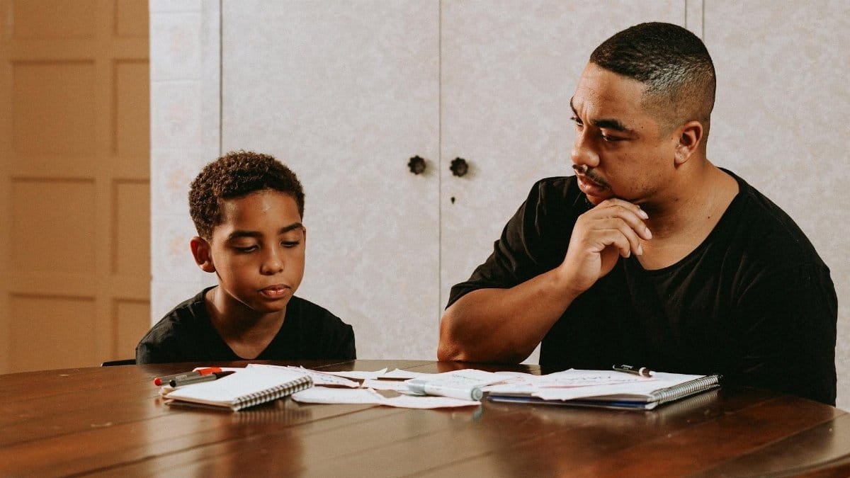 A father helps his son with homework at a table, fostering learning and connection.