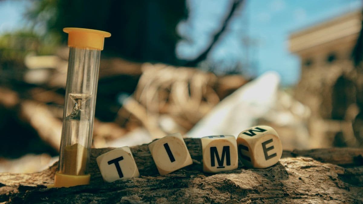 Hourglass and wooden blocks with letters spelling 'TIME' on a sunny day outdoors.