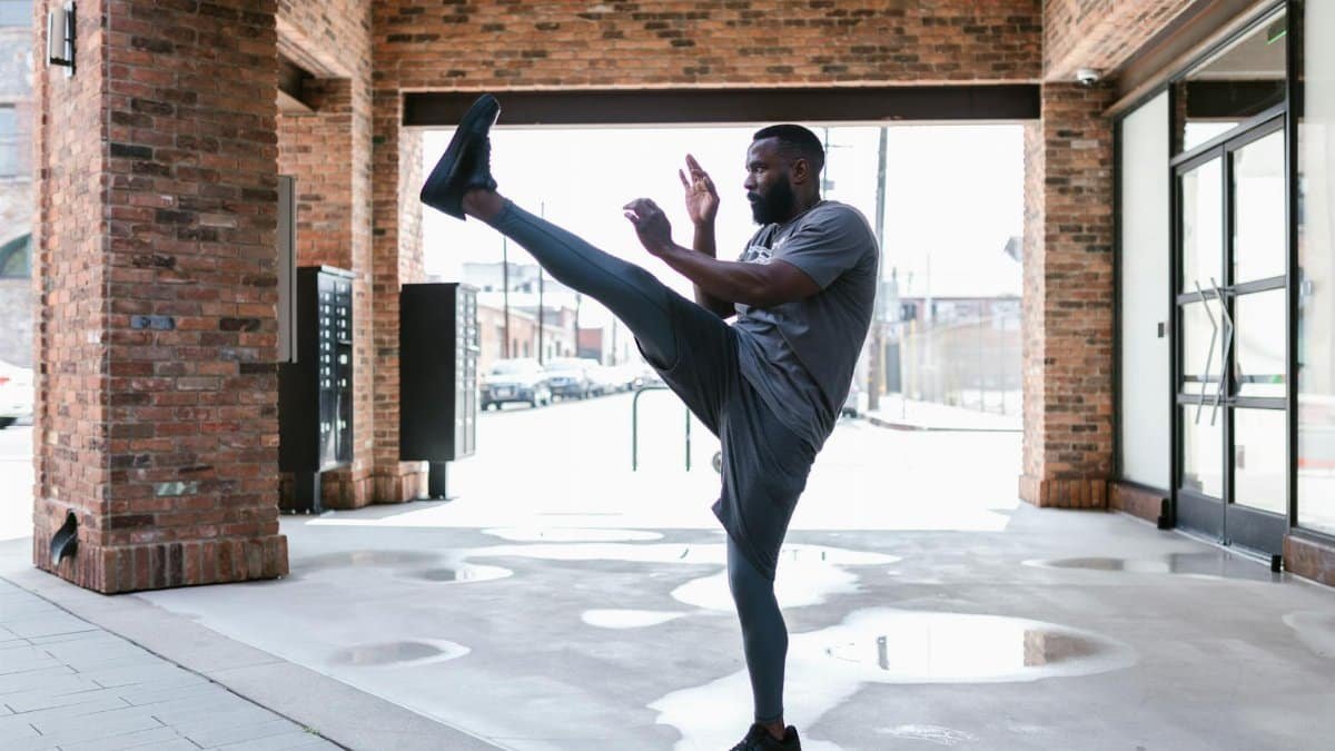 Athletic man executing a high kick in an urban environment, embodying fitness and discipline.
