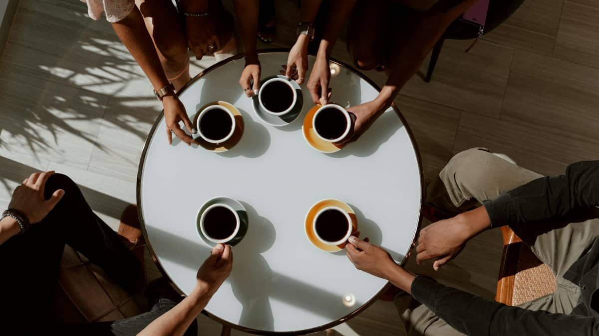A group of friends enjoying coffee around a café table in a warm setting.