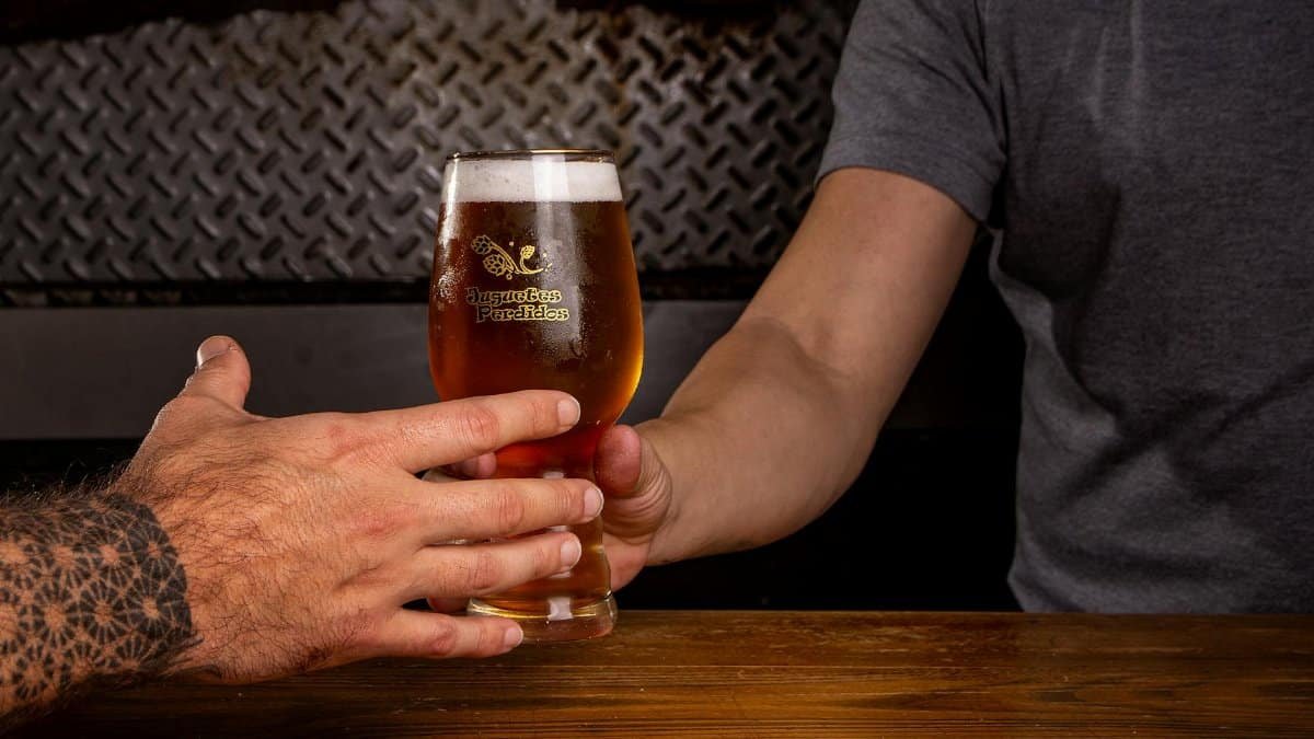 Two hands exchanging a beer glass at a bar, showcasing community and craftsmanship.