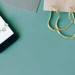 Illustration of online payment with smartphone, credit card, and shopping bag on mint background.