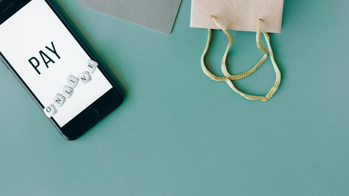 Illustration of online payment with smartphone, credit card, and shopping bag on mint background.