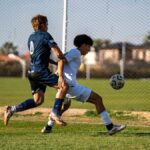 Two players competing in a heated soccer match outdoors on a sunny day.