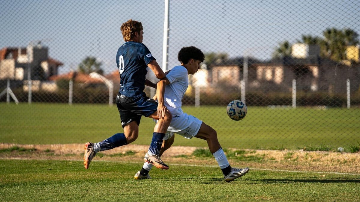 Two players competing in a heated soccer match outdoors on a sunny day.