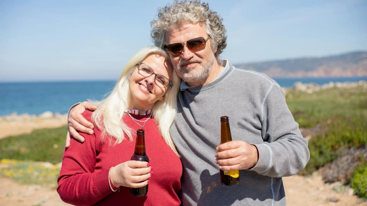 Happy couple drinking beer together on a sunny day by the ocean in Portugal.