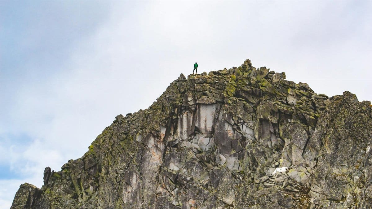 A lone hiker stands atop a rugged mountain peak against the sky, capturing a moment of adventure.