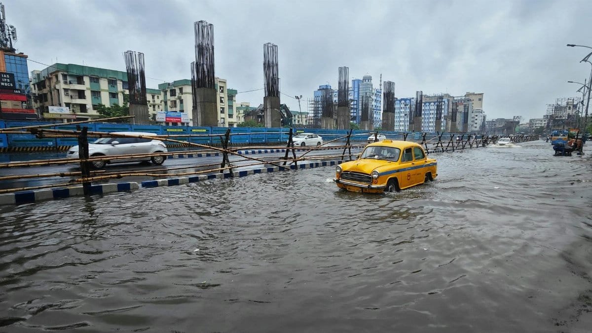 A flooded urban street in Kolkata with a classic yellow taxi navigating through the waterlogged road.