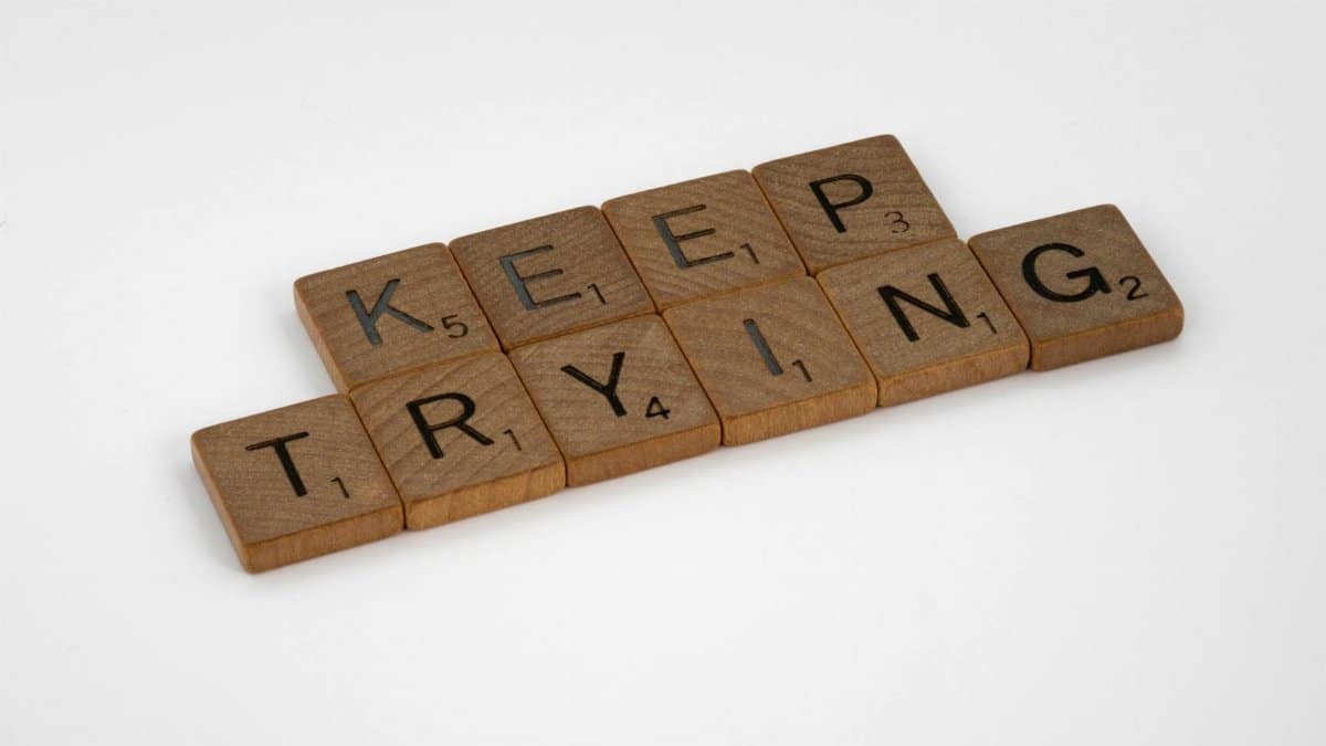 Scrabble tiles form an inspiring message 'Keep Trying' on a white background. Motivational and clean aesthetic.