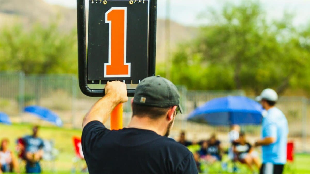 Back view of anonymous male trainer standing near scoreboard on blurred background of field during sports competition