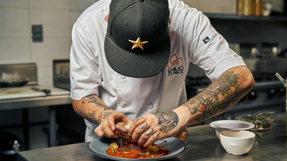 Tattooed chef expertly plates a gourmet dish with precision and skill in a restaurant kitchen.
