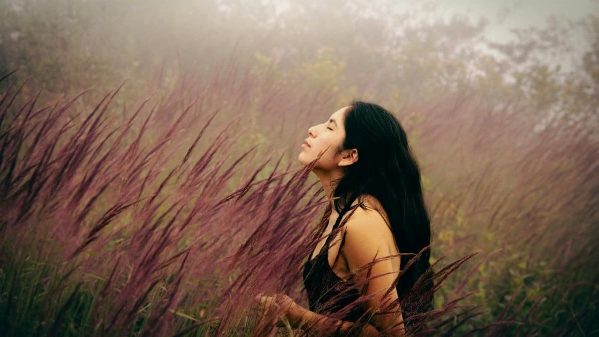 A serene young woman with eyes closed, basking in a mist-covered meadow, immersed in nature.
