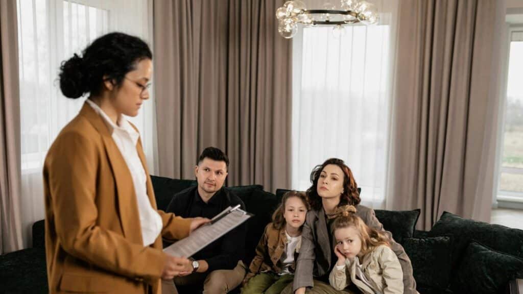 Realtor discusses documents with family sitting on sofa in modern living room.