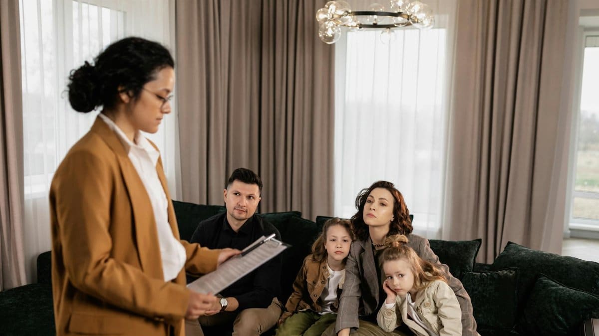 Realtor discusses documents with family sitting on sofa in modern living room.