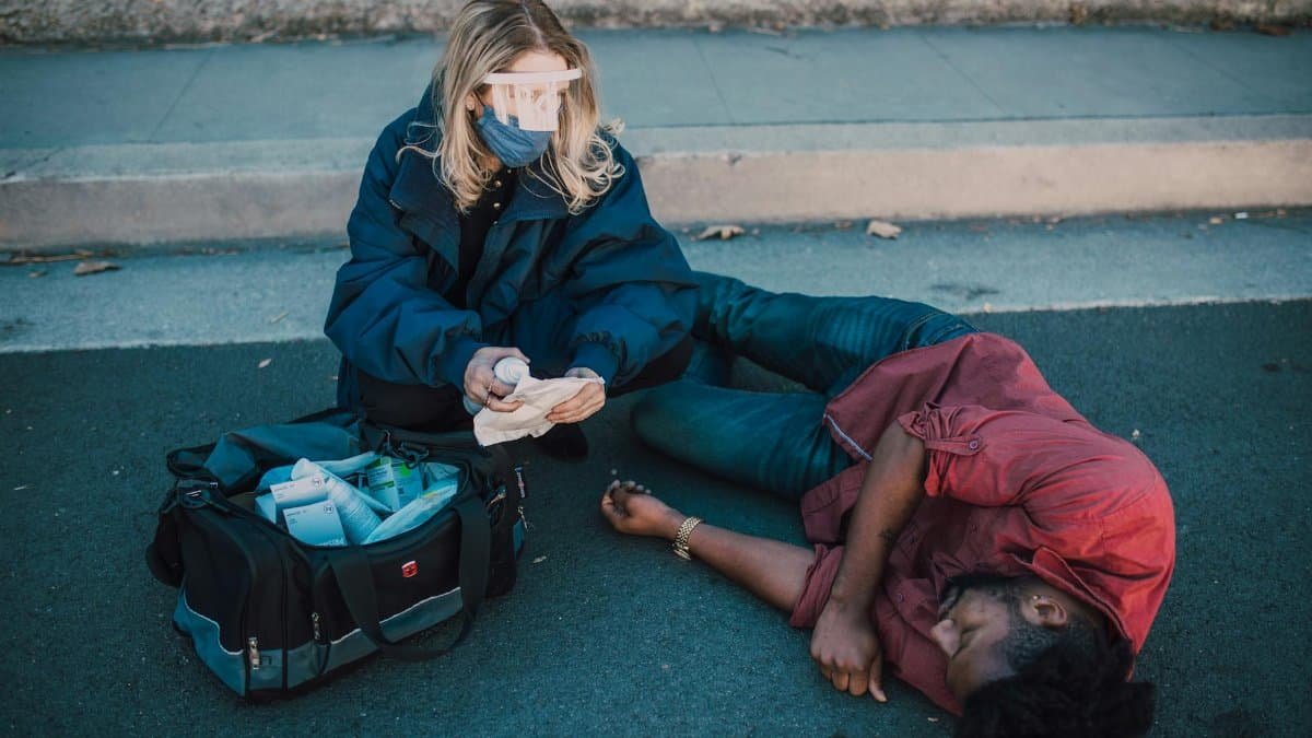 A paramedic tends to an unconscious man on a road, highlighting emergency services.