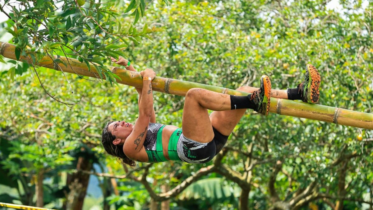 Woman athlete tackling a bamboo climb in an outdoor adventure race under a lush canopy.