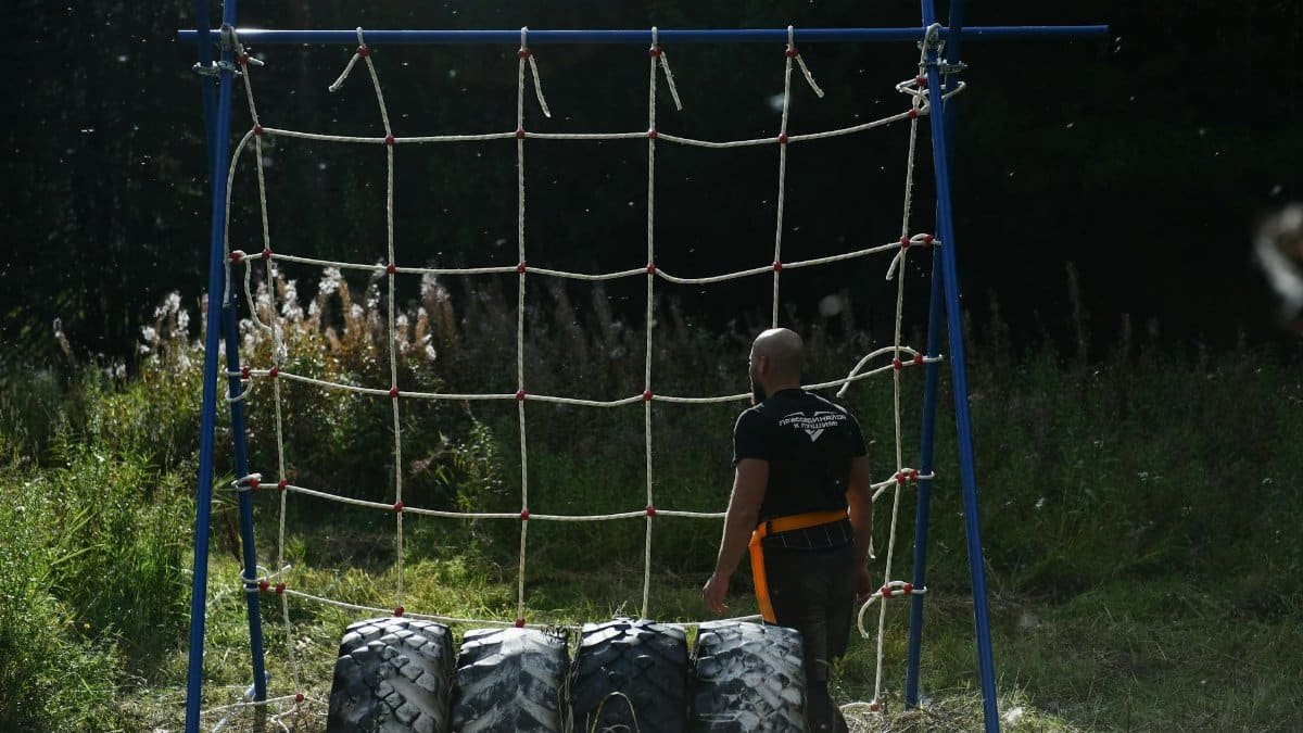 Man training on an outdoor obstacle course, featuring a climbing net and tires.