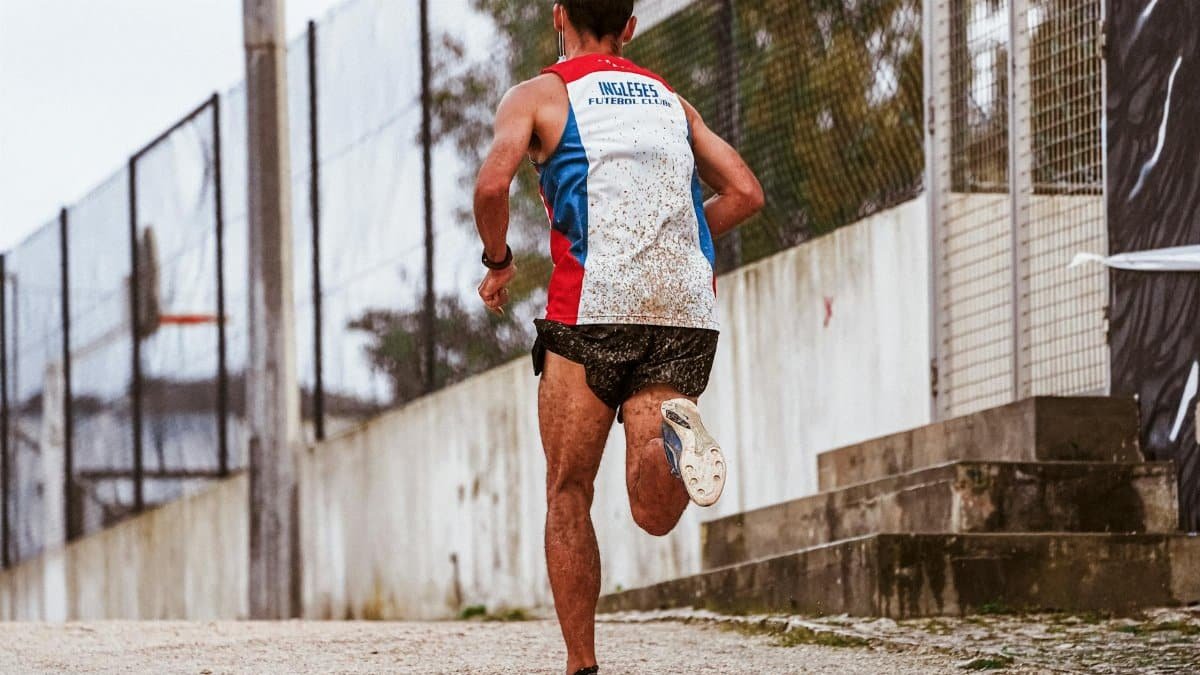 Rear view of a male runner sprinting outdoors on a gravel pathway in sportswear.