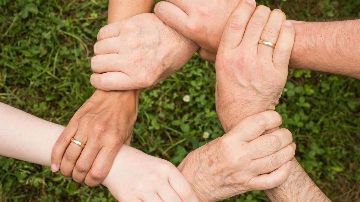 Close-up of diverse hands forming a connection, symbolizing teamwork and unity outdoors.
