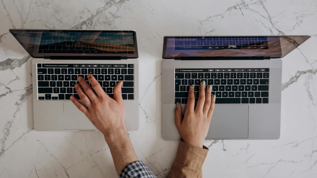 Top view of hands typing on two laptops, showcasing collaboration and technology.