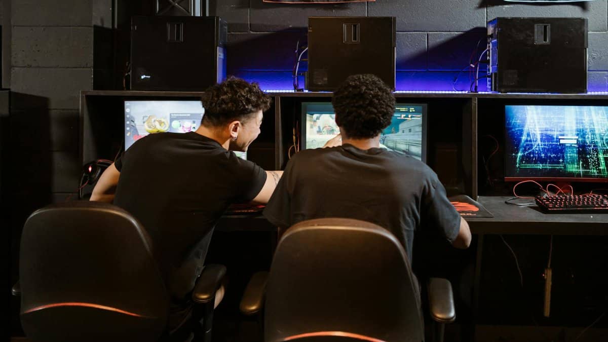 Two young men engaged in intense gaming session at an eSports venue. Computers and ambient lighting create an immersive experience.