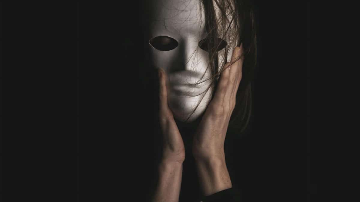 An eerie, dramatic portrayal of a person clutching a white mask, enveloped in darkness.
