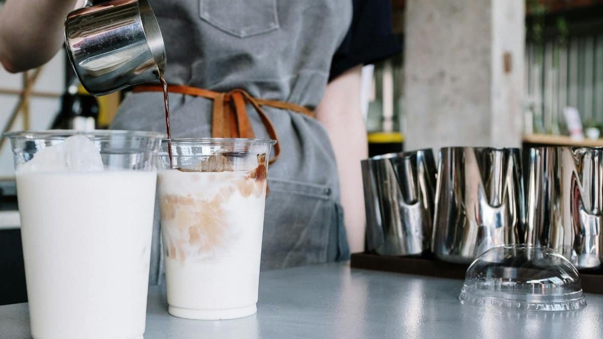 Close-up of a barista crafting iced lattes in a trendy indoor café setting.
