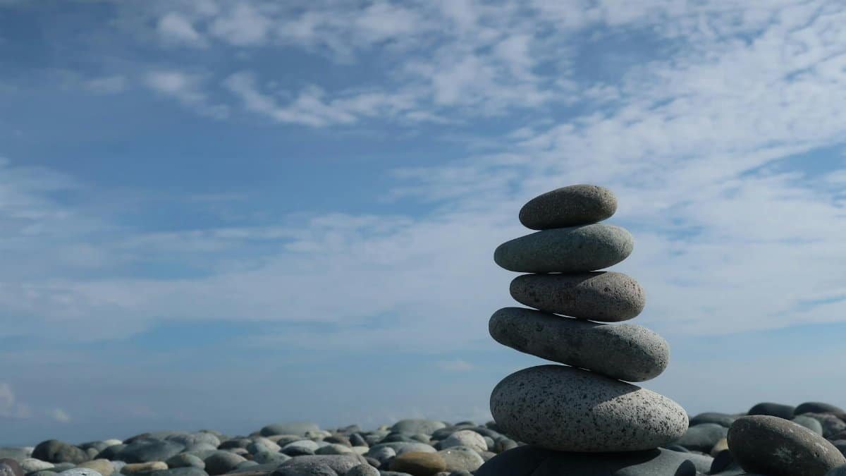 A tranquil scene of a balanced stone stack on a pebble beach under a bright blue sky.