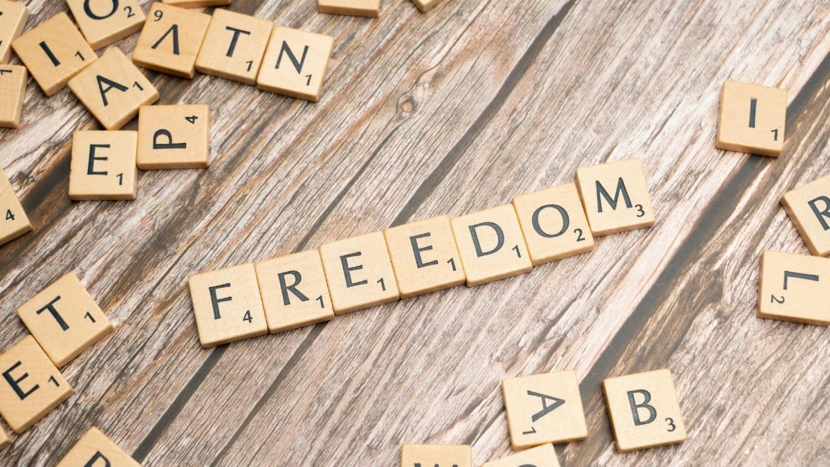 Scrabble tiles arranged to spell 'Freedom' on a rustic wooden surface, conveying a conceptual theme.