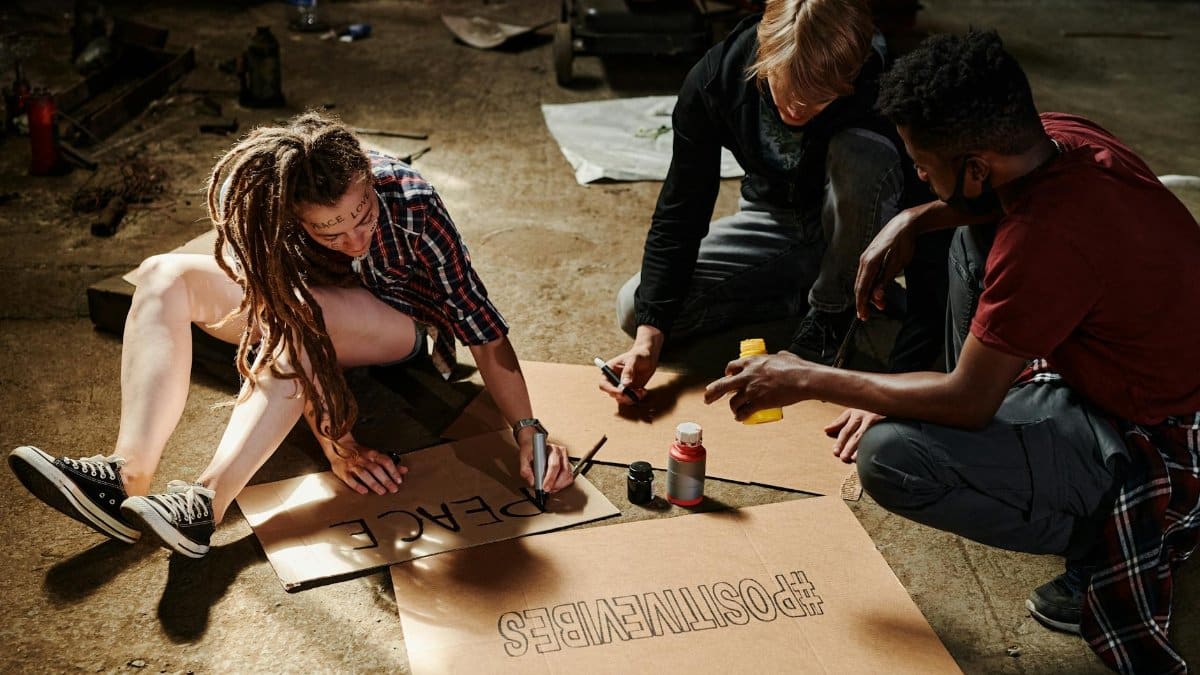 Three young activists creatively crafting protest signs indoors on cardboard, fostering peace and positivity.