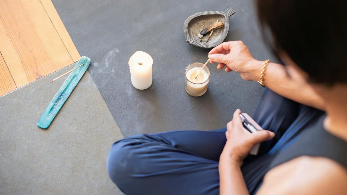 A person engages in a calming ritual with candles and palo santo, creating a serene atmosphere.