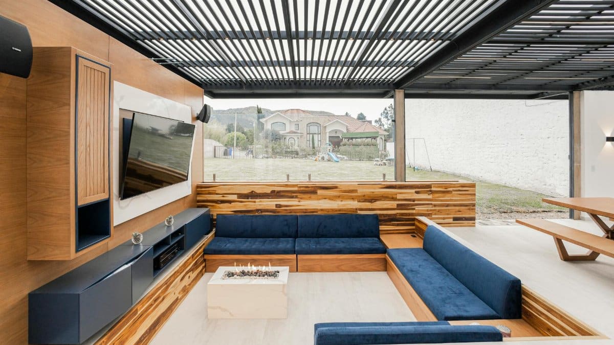 Contemporary outdoor living room featuring a cozy blue sofa, wooden accents, and glass wall.