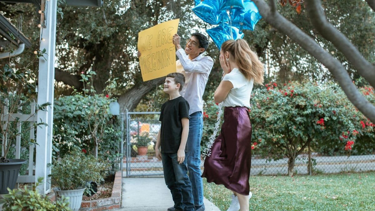 Family joyfully reveals pregnancy in a garden setting with balloons.