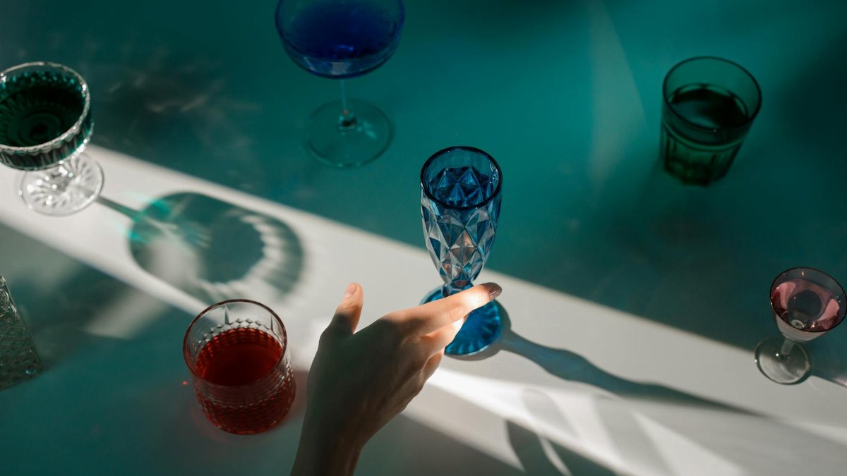 A minimalist still life featuring colorful drinks in elegant glassware with dramatic lighting.