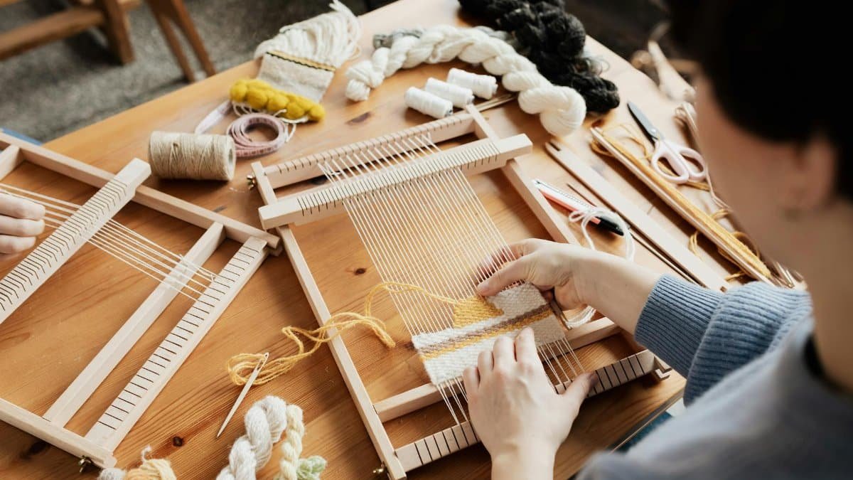 A person weaving textiles using a wooden hand loom, showcasing creativity and craftsmanship.