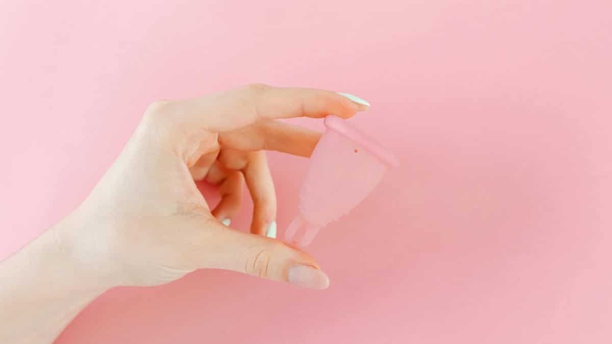 A close-up of a hand holding a menstrual cup against a pink background, symbolizing menstrual health.