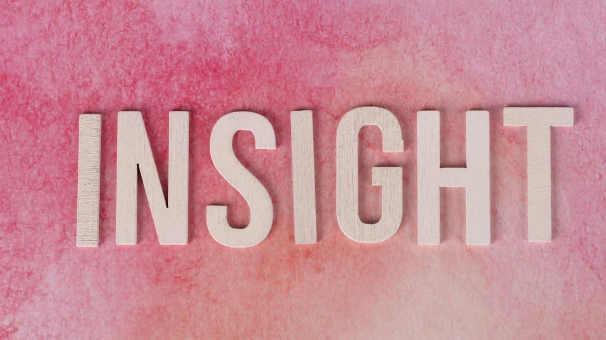 Wooden letters spelling INSIGHT on a pink watercolor background.