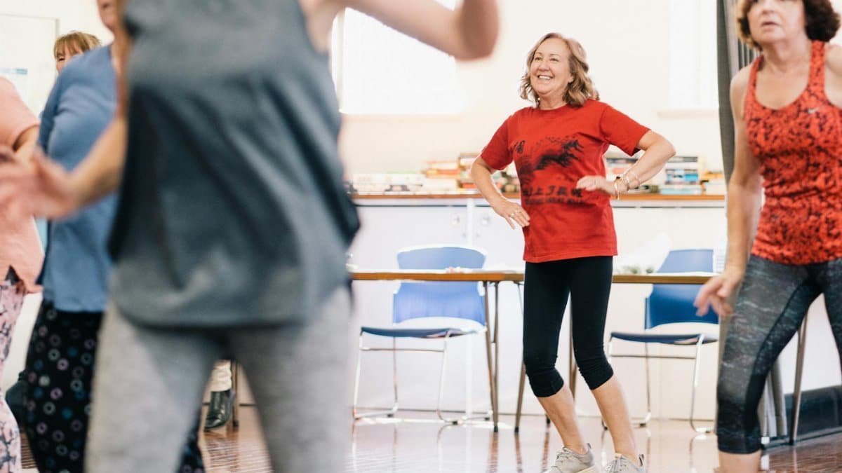A vibrant dance class indoors with smiling women, encouraging a healthy lifestyle.